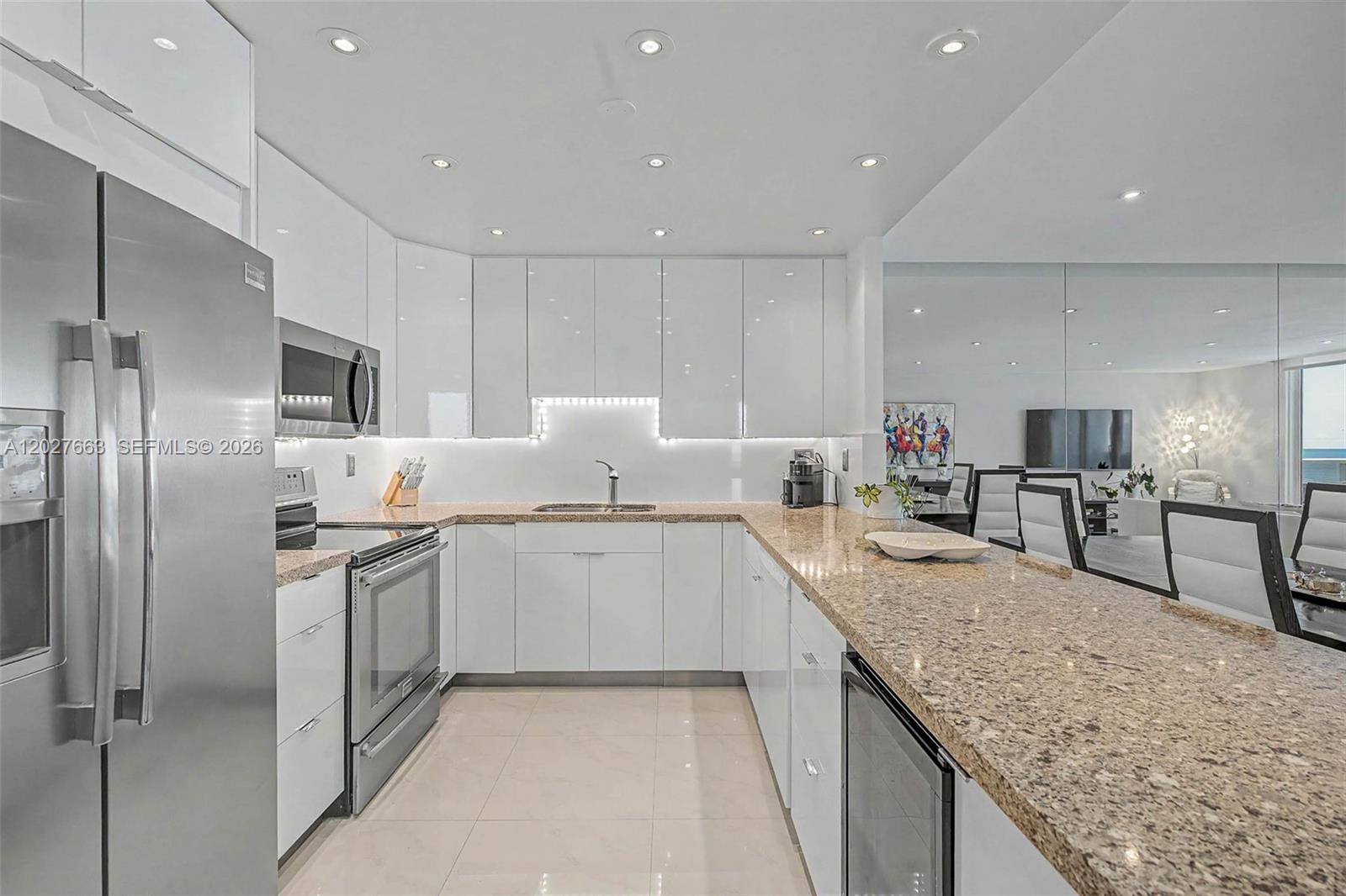 A modern kitchen features white glossy cabinets, granite countertops, stainless steel appliances, and recessed lighting — 2301 Collins Ave # 1210, Miami Beach FL 33139, MIAMI BEACH, FL