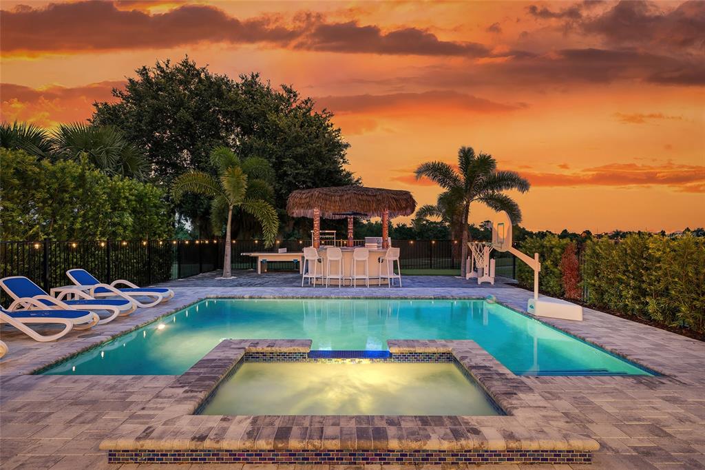 A backyard swimming pool and hot tub feature a tiki bar under a sunset sky — 801 GOLDEN BEAR DRIVE, KISSIMMEE, FL