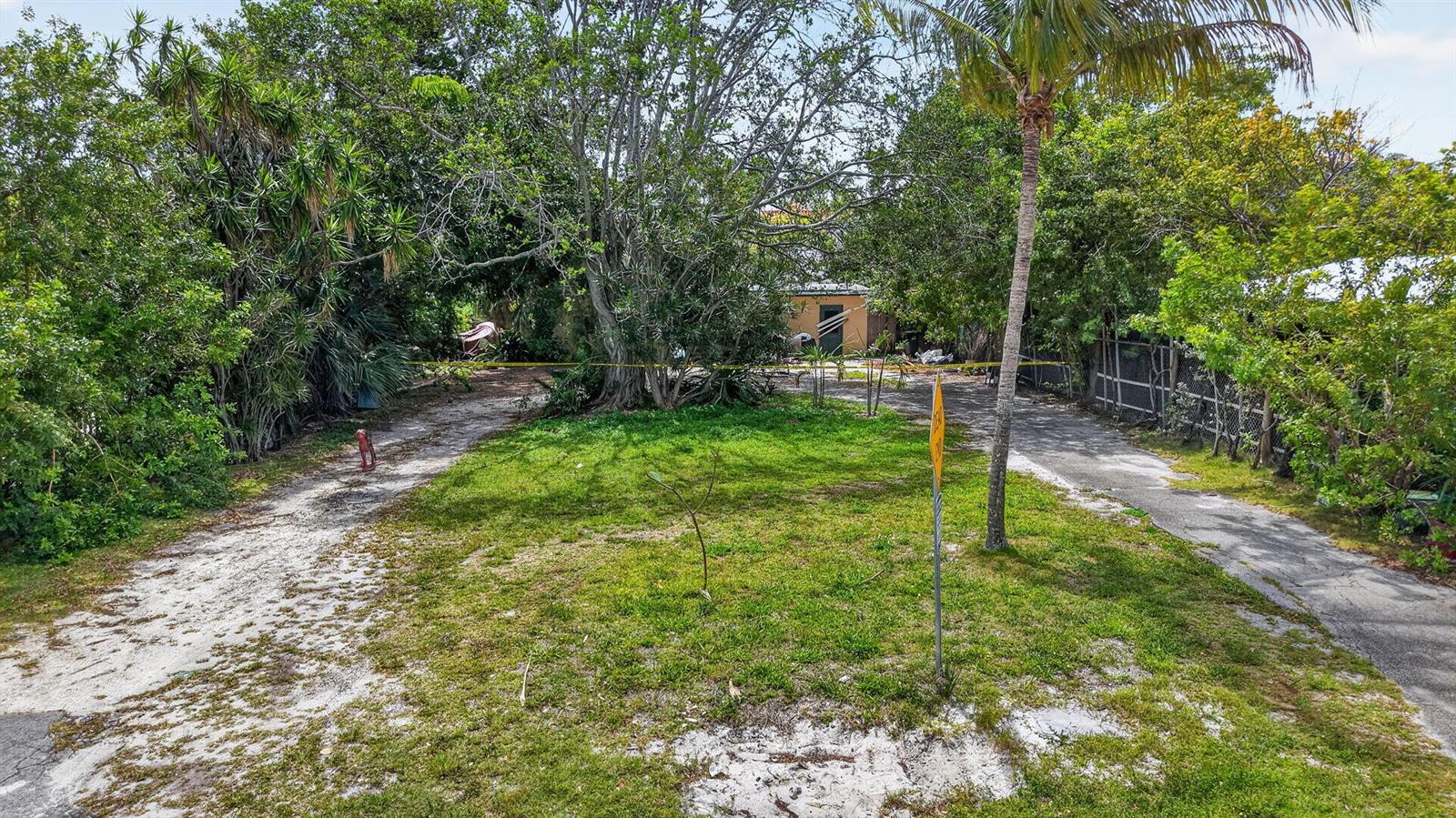 A grassy, tree-lined lot features a dirt driveway and a yellow building in the background — 600 Allen Avenue, Delray Beach FL 33483, DELRAY BEACH, FL