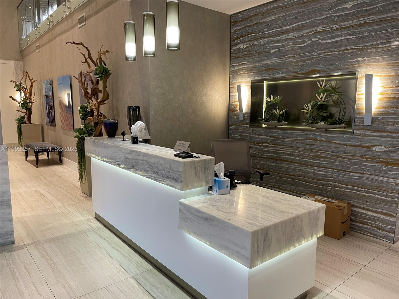 A modern reception area features a white marble desk, ambient lighting, and decorative wall art — 2301 S Ocean Dr # 607, Hollywood FL 33019, HOLLYWOOD, FL