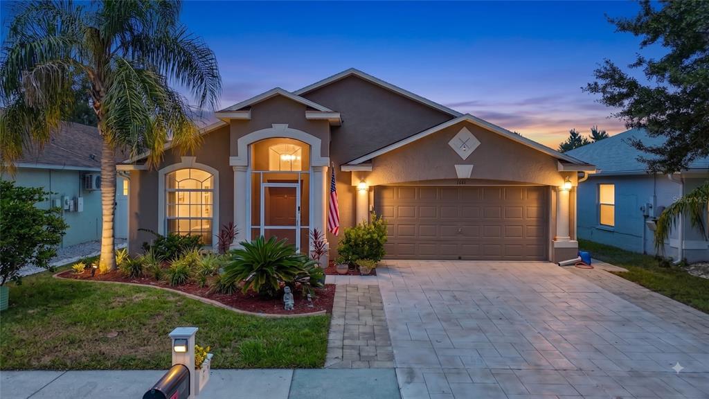 A single-story house with a tan stucco exterior, a two-car garage, and a paved driveway — 7441 TOWER BRIDGE DRIVE, WESLEY CHAPEL, FL