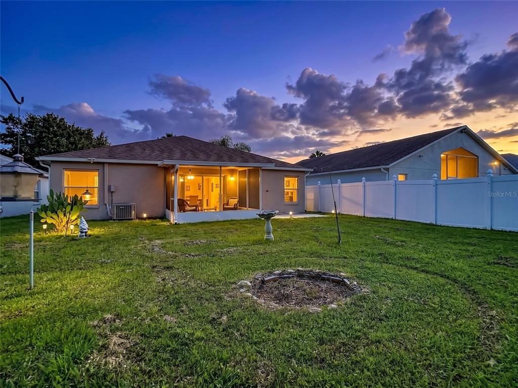 A backyard view of a house with a screened-in porch, lawn, and white vinyl fence — 7441 TOWER BRIDGE DRIVE, WESLEY CHAPEL, FL