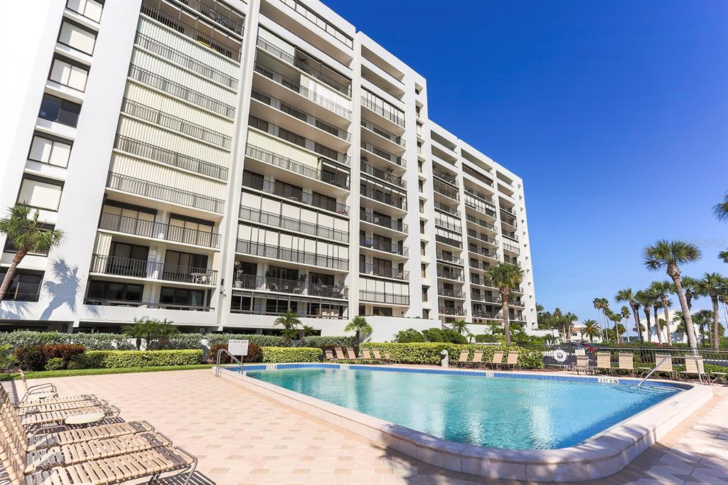 A multi-story apartment building stands behind a swimming pool with lounge chairs on the deck — 1460 GULF BLVD UNIT 412, CLEARWATER BEACH, FL