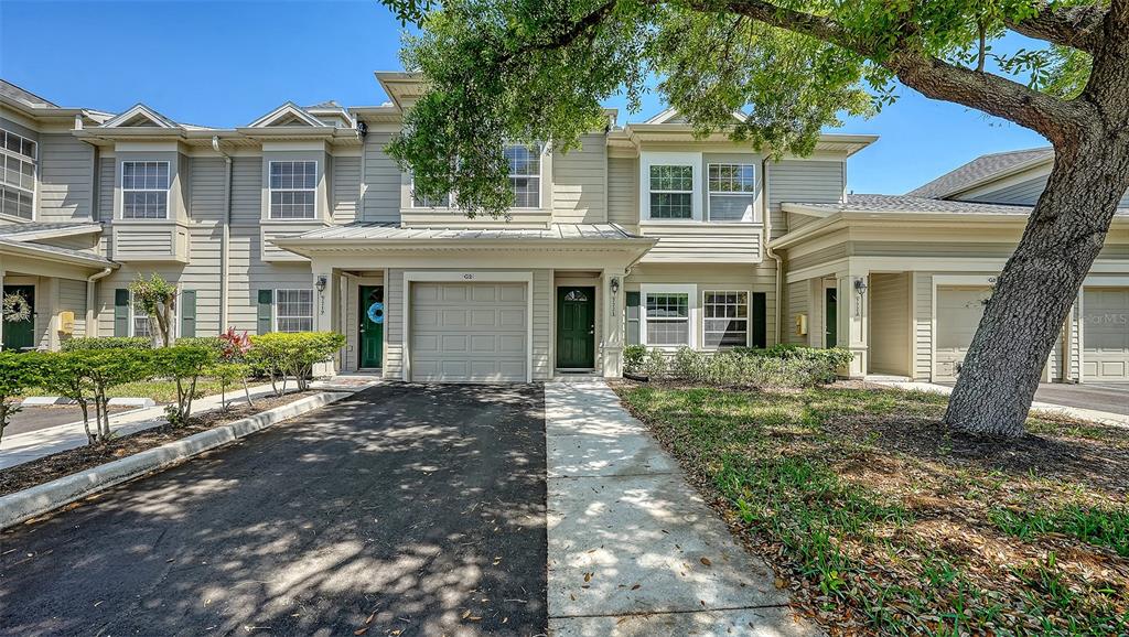 A two-story townhouse exterior features a garage, a front door, and a large shade tree — 7721 PLANTATION CIRCLE, BRADENTON, FL