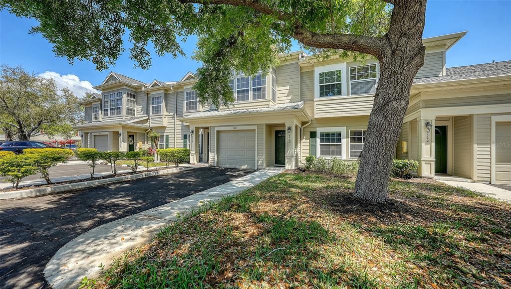 A two-story townhouse exterior features light siding, a garage, and a large shade tree — 7721 PLANTATION CIRCLE, BRADENTON, FL