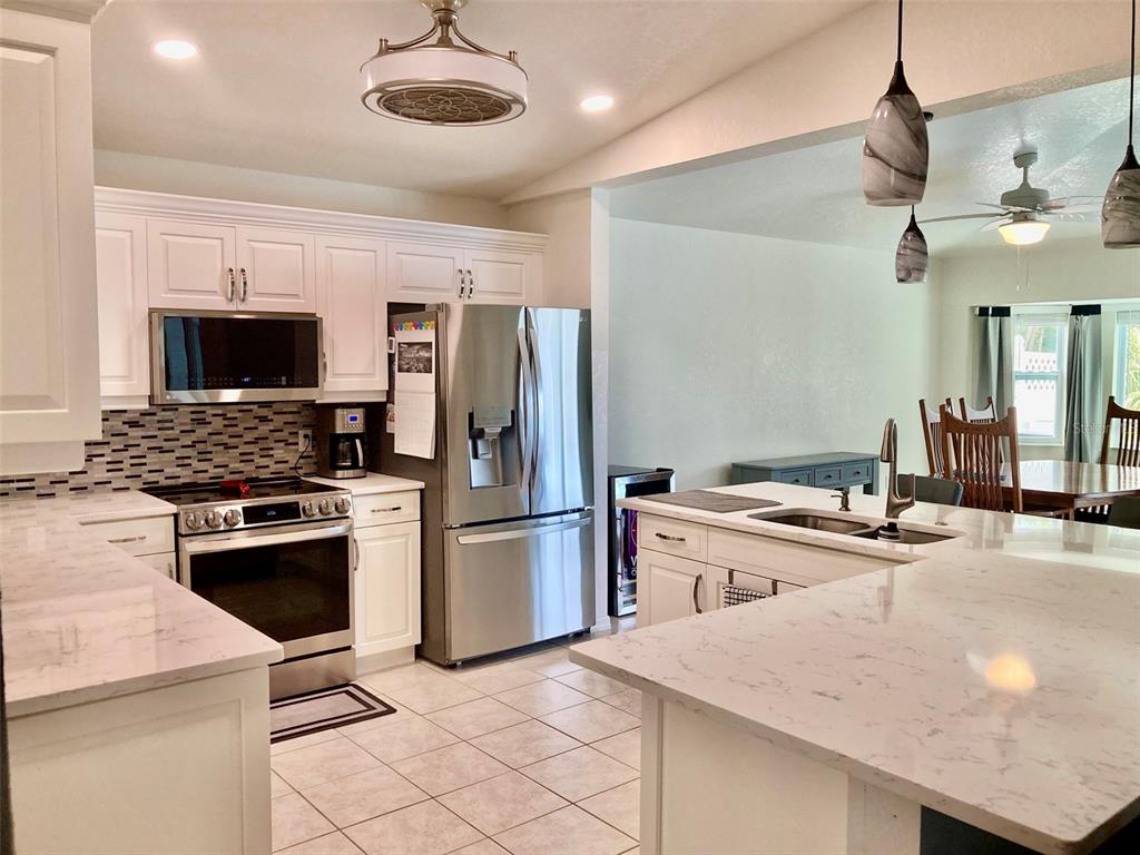 A kitchen features white cabinets, stainless steel appliances, a marble-look island, and tile flooring — 123 KINGS DRIVE, ROTONDA WEST, FL