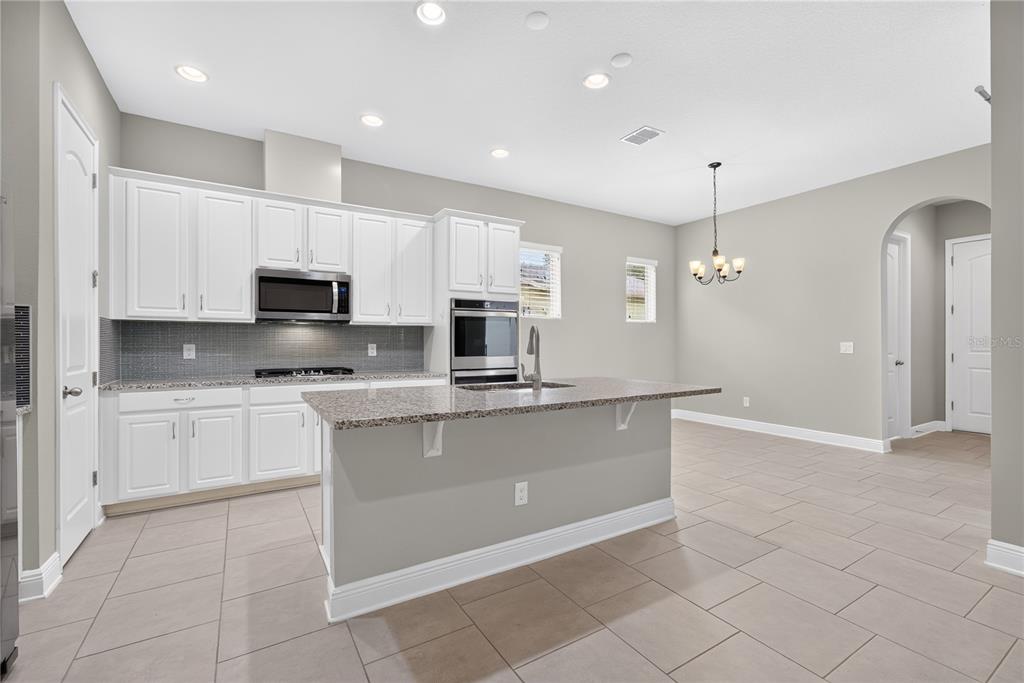 A kitchen features white cabinets, granite countertops, a center island, and light-colored tile flooring — 16954 TRADEWIND POINT, WINTER GARDEN, FL