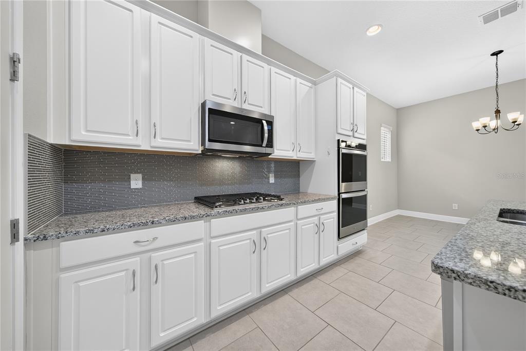 A kitchen with white cabinets, granite countertops, stainless steel appliances, and a gray tiled backsplash — 16954 TRADEWIND POINT, WINTER GARDEN, FL