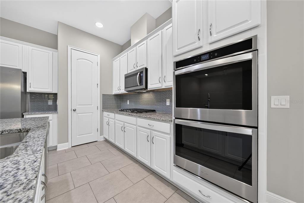 A kitchen with white cabinets, stainless steel double wall ovens, and granite countertops — 16954 TRADEWIND POINT, WINTER GARDEN, FL