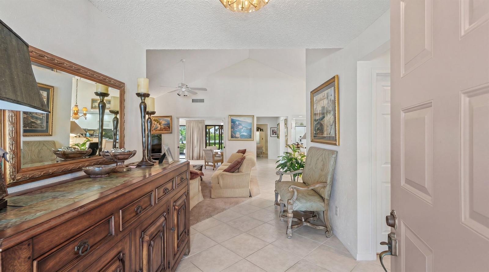 An entryway with a wooden sideboard leads into a living room with vaulted ceilings — 16997 Freshwind Circle, Jupiter FL 33477, JUPITER, FL