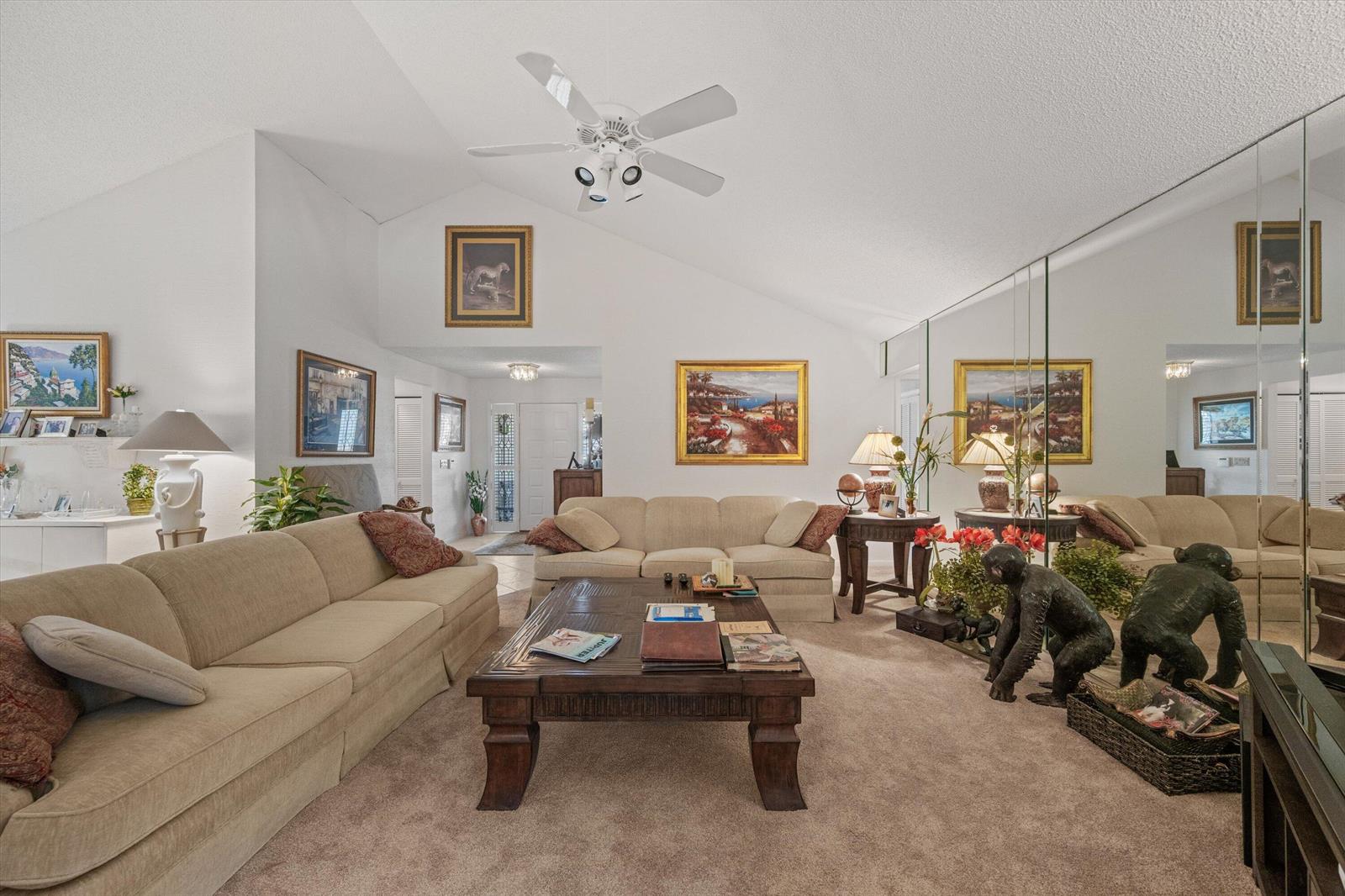 A living room features a vaulted ceiling, beige sofas, a wooden coffee table, and mirrored walls — 16997 Freshwind Circle, Jupiter FL 33477, JUPITER, FL