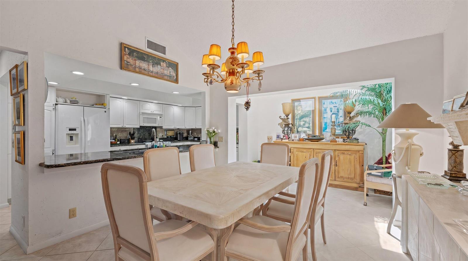 A dining room with a stone table, upholstered chairs, and a chandelier, adjacent to a kitchen — 16997 Freshwind Circle, Jupiter FL 33477, JUPITER, FL