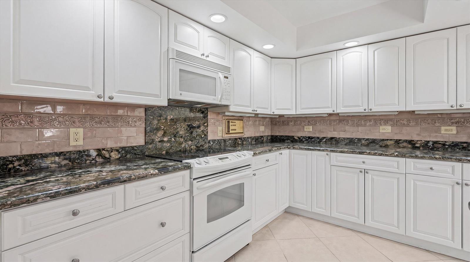 A kitchen with white cabinets, dark granite countertops, and a pink subway tile backsplash — 16997 Freshwind Circle, Jupiter FL 33477, JUPITER, FL