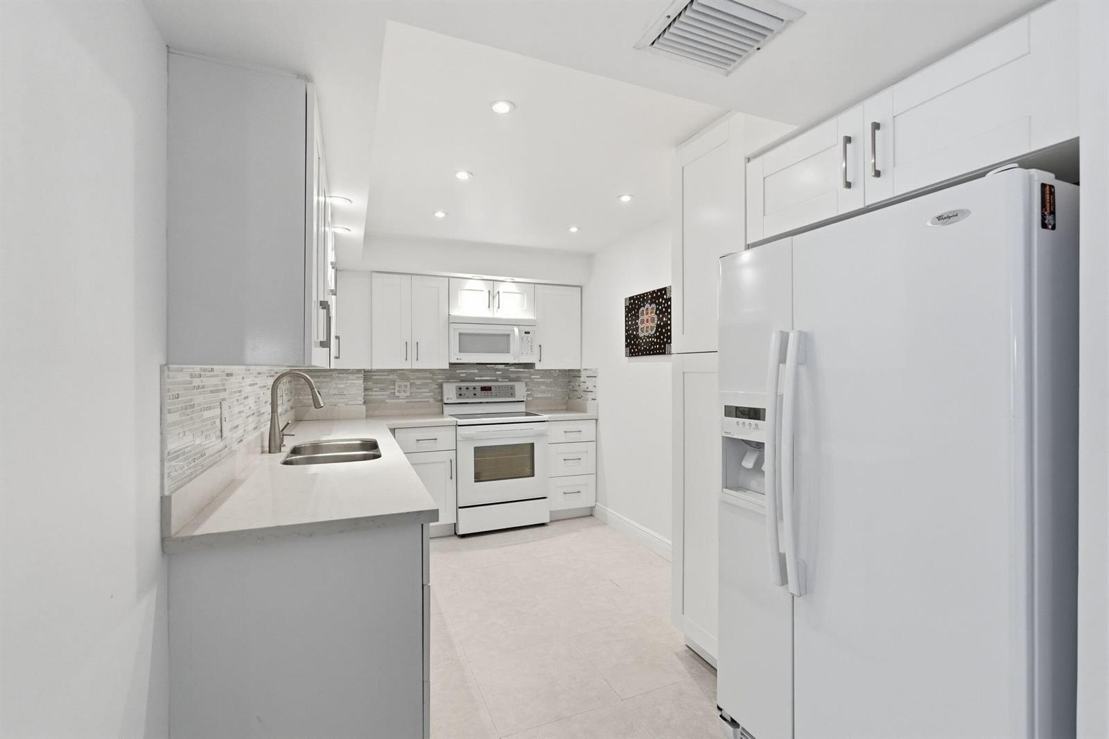 A white kitchen features light countertops, a tiled backsplash, and stainless steel appliances — 3450 S Ocean Boulevard # 121, Palm Beach FL 33480, PALM BEACH, FL