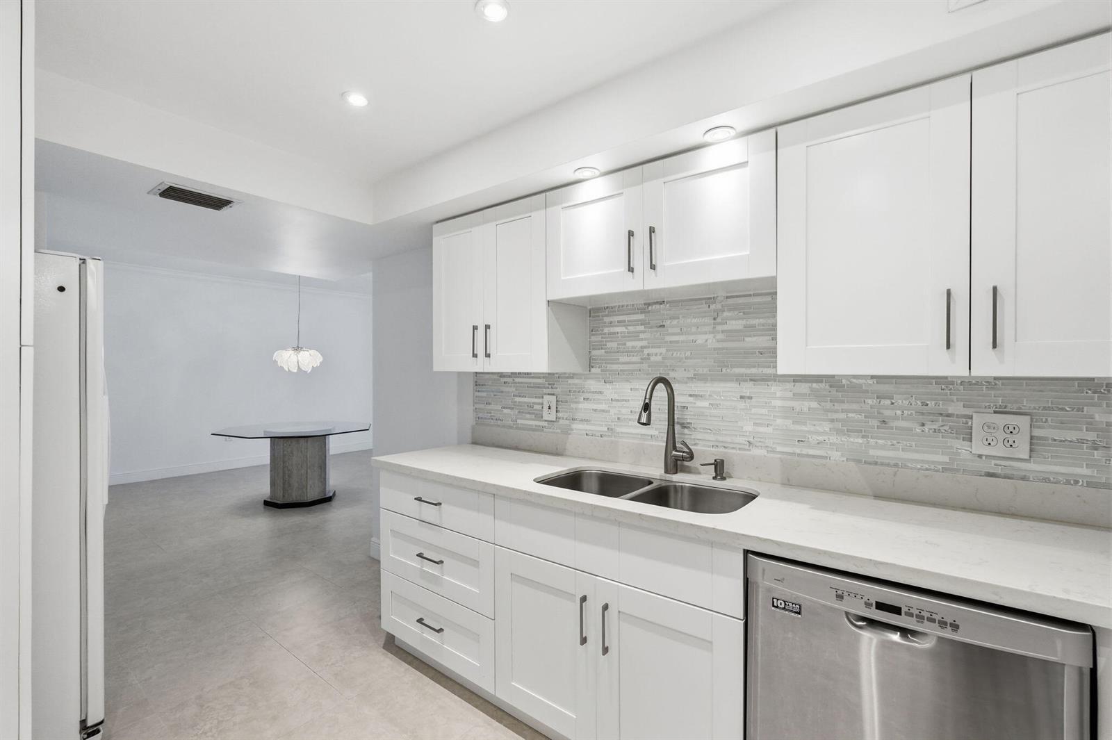 A kitchen with white cabinets, light countertops, a tiled backsplash, and a stainless steel dishwasher — 3450 S Ocean Boulevard # 121, Palm Beach FL 33480, PALM BEACH, FL