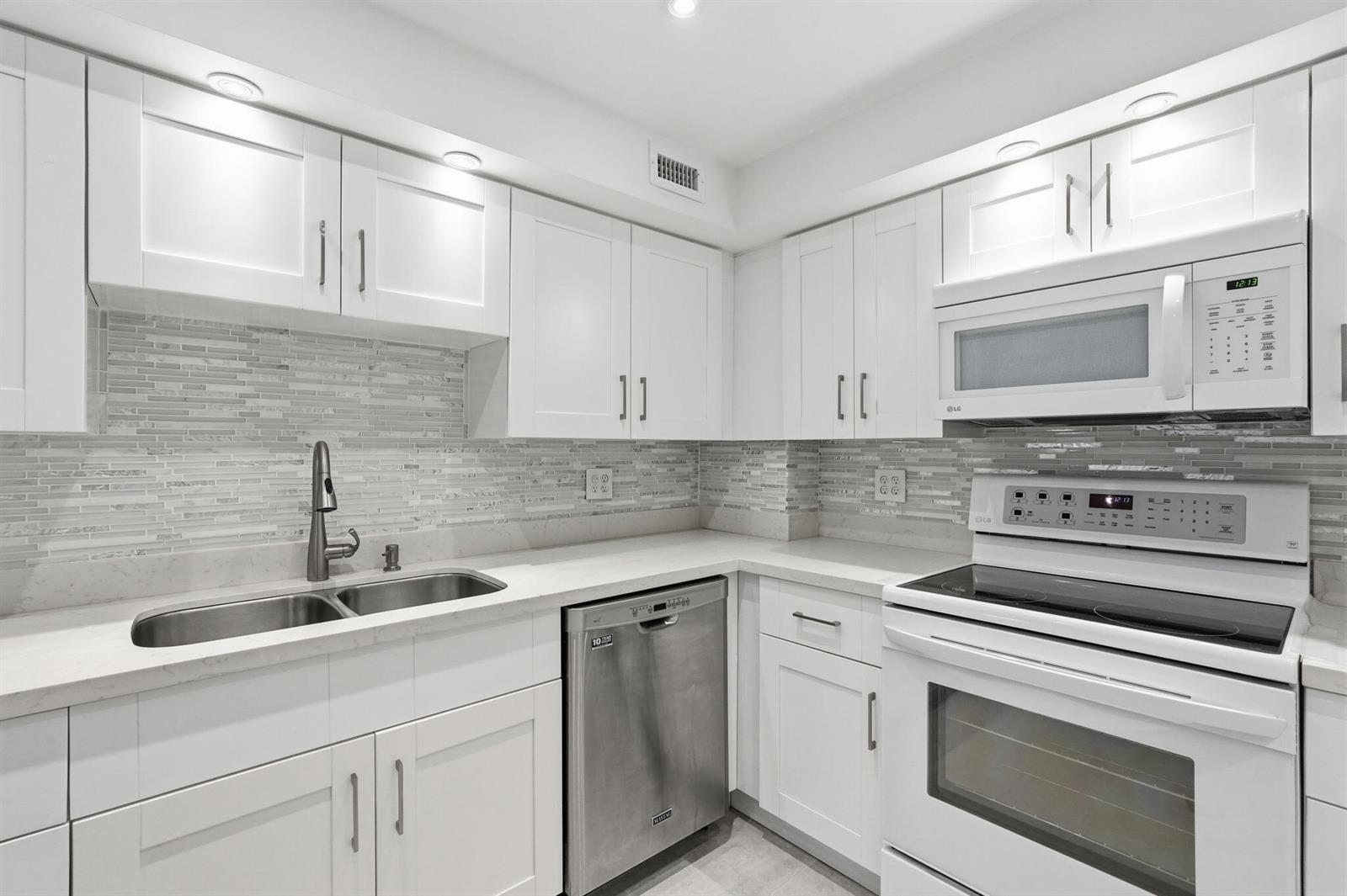 A modern kitchen features white cabinets, stainless steel appliances, and a gray tiled backsplash — 3450 S Ocean Boulevard # 121, Palm Beach FL 33480, PALM BEACH, FL