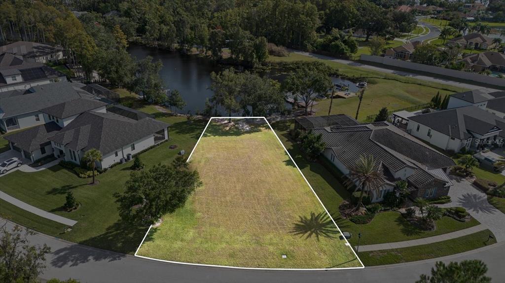 An aerial view shows a vacant, trapezoidal residential lot situated between two houses near a lake — 3926 COVE LAKE PLACE, LAND O LAKES, FL
