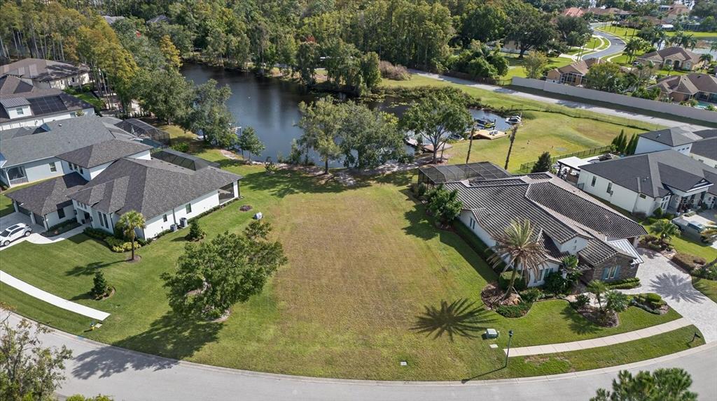 An aerial view shows a vacant residential lot situated between two houses near a lake — 3926 COVE LAKE PLACE, LAND O LAKES, FL