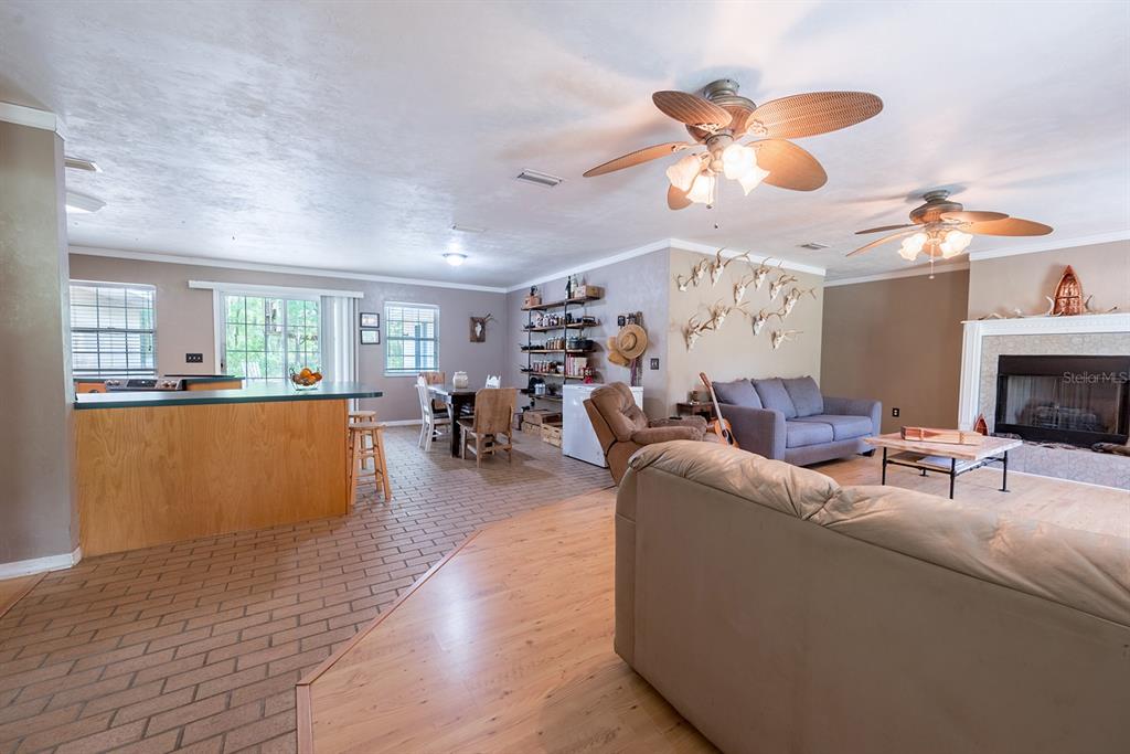 An open-concept living and dining area features brick flooring, wood-look laminate, and a stone fireplace — 5876 SW 52ND TERRACE, LAKE BUTLER, FL