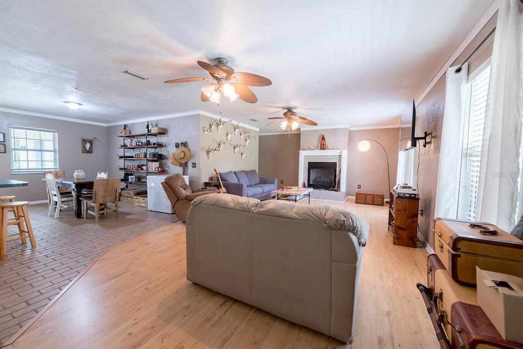 An open-concept living and dining area features wood-look flooring, a fireplace, and ceiling fans — 5876 SW 52ND TERRACE, LAKE BUTLER, FL