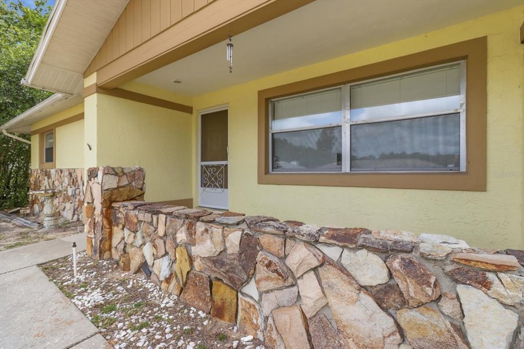 A yellow house exterior features a stone-faced porch wall and a white screen door — 3454 N HONEYLOCUST DRIVE, BEVERLY HILLS, FL