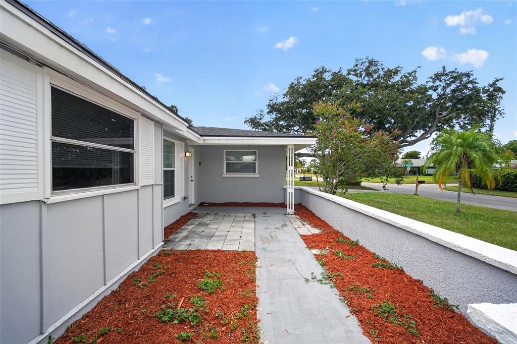 A gray house exterior features a covered entryway, a tiled patio, and red mulch landscaping — 3834 WARREN RIDGE STREET, SARASOTA, FL