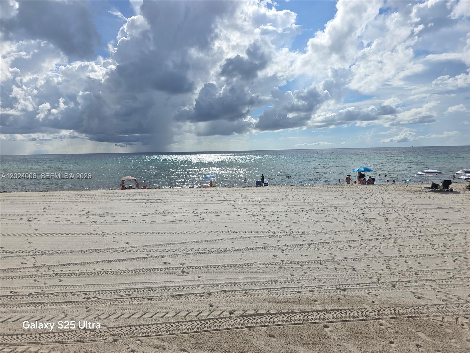 A wide, sandy beach features tire tracks, several umbrellas, and people under a cloudy sky — 3725 S Ocean Dr # 617, Hollywood FL 33019, HOLLYWOOD, FL