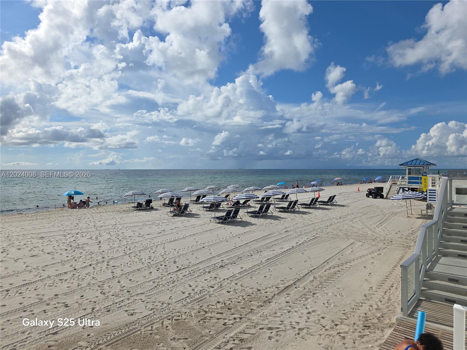 A sandy beach features rows of blue and white umbrellas and lounge chairs near stairs — 3725 S Ocean Dr # 617, Hollywood FL 33019, HOLLYWOOD, FL