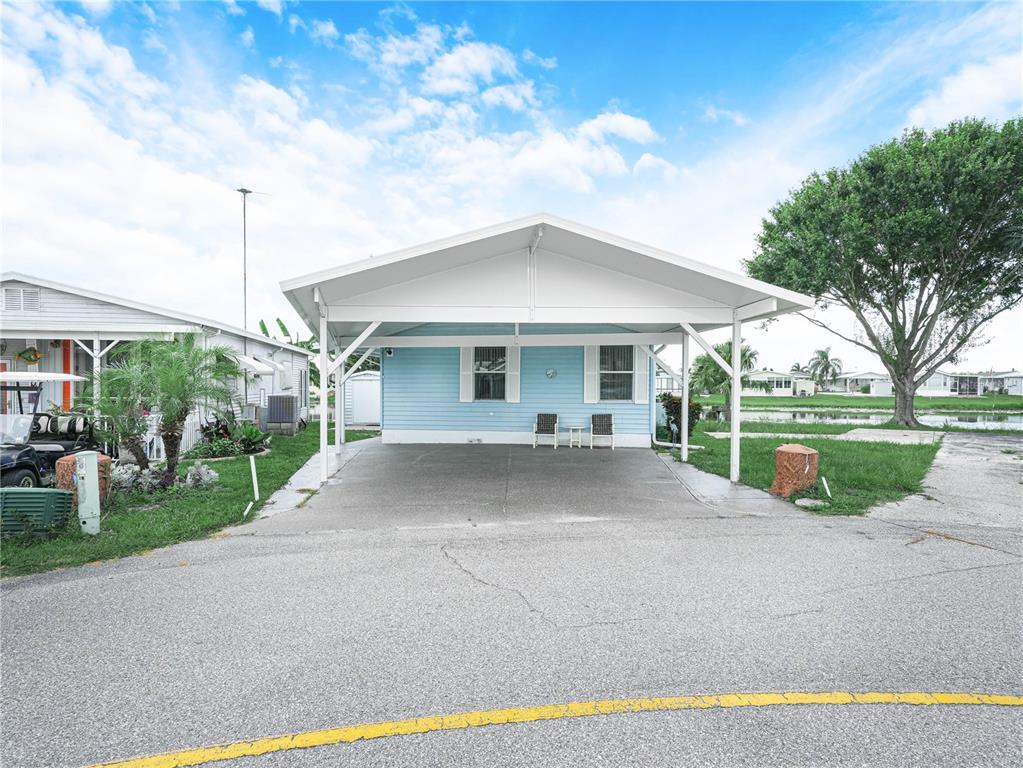 A light blue mobile home features a large attached carport and a concrete driveway — 17 RED QUILL CIRCLE, LAKE WALES, FL