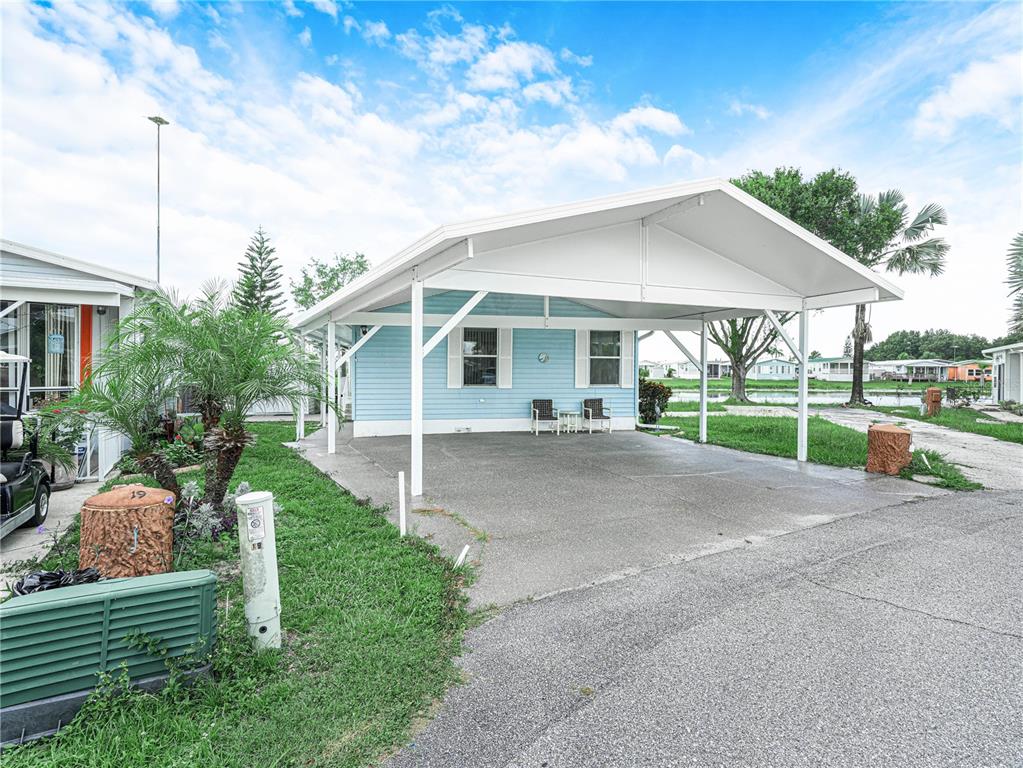 A light blue mobile home features a large white carport and a concrete driveway — 17 RED QUILL CIRCLE, LAKE WALES, FL