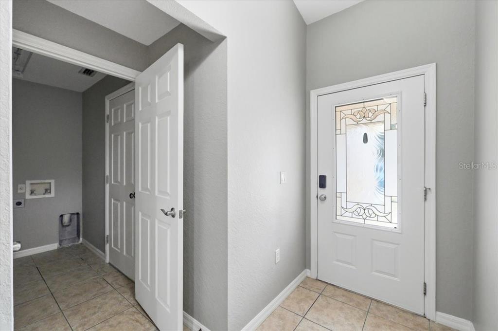 An entryway with tiled floors, a white front door, and an adjacent laundry room — 4757 ACORN DRIVE, MULBERRY, FL