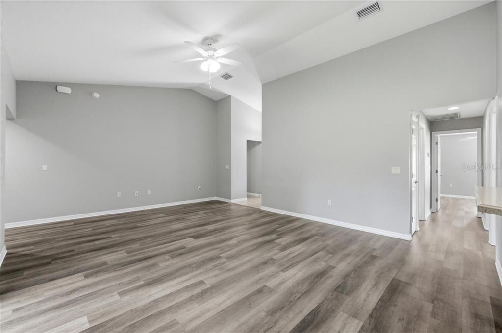 An empty living room features vaulted ceilings, light gray walls, and wood-look vinyl plank flooring — 4757 ACORN DRIVE, MULBERRY, FL