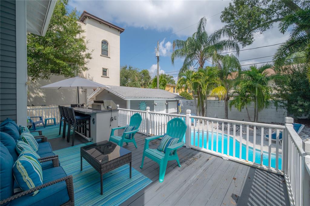 An elevated wooden deck features outdoor seating, a grill station, and a view of a pool — 2921 W EL PRADO BOULEVARD, TAMPA, FL