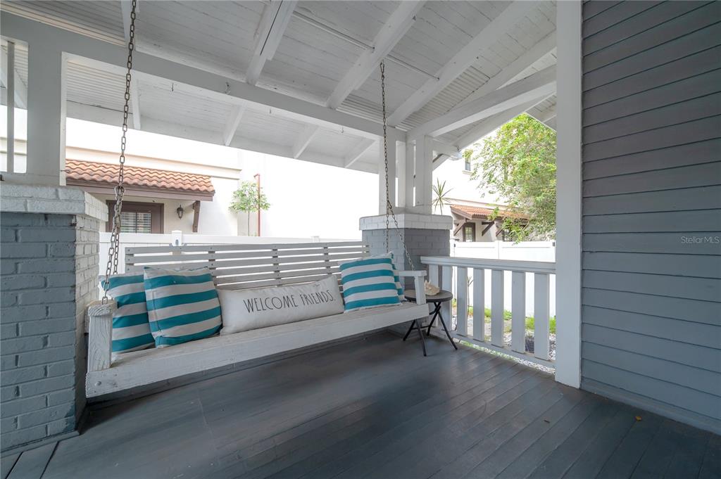 A covered porch features a white wooden swing with striped pillows and gray flooring — 2921 W EL PRADO BOULEVARD, TAMPA, FL