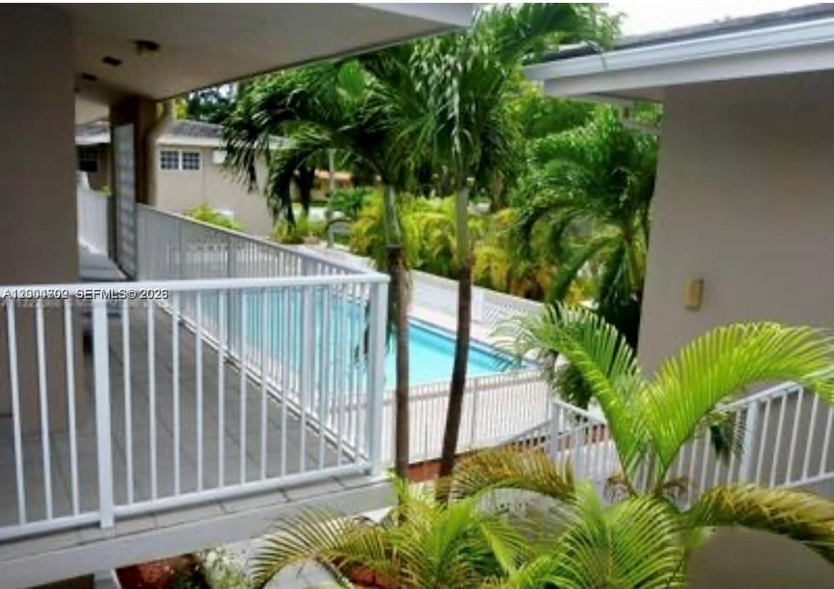 An elevated balcony overlooks a swimming pool surrounded by palm trees and white fencing — 6565 Santona St, Coral Gables FL 33146, CORAL GABLES, FL