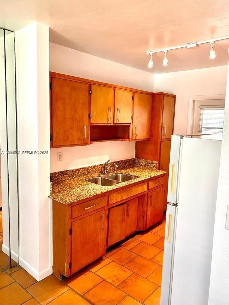 A kitchen features wooden cabinets, granite countertops, a double sink, and terracotta floor tiles — 6565 Santona St, Coral Gables FL 33146, CORAL GABLES, FL
