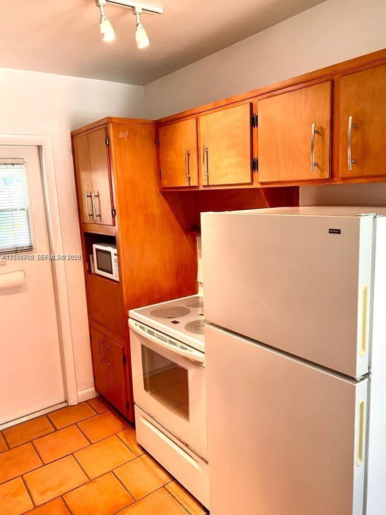 A kitchen features wood cabinets, a white stove, a white refrigerator, and tile flooring — 6565 Santona St, Coral Gables FL 33146, CORAL GABLES, FL