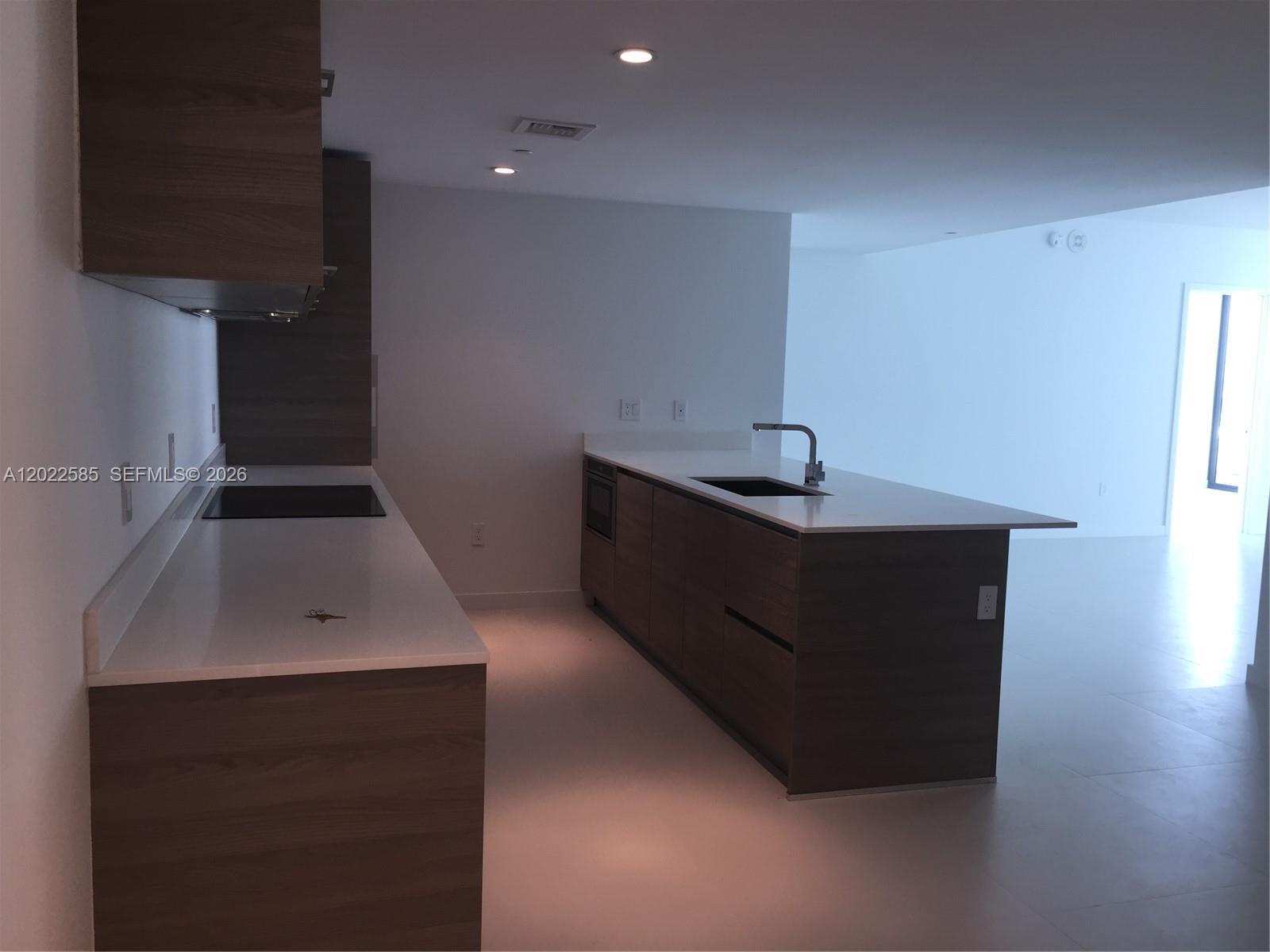 A modern kitchen features dark wood cabinetry, white countertops, and a central island with a sink — 1300 S Miami # 1910, Miami FL 33130, MIAMI, FL
