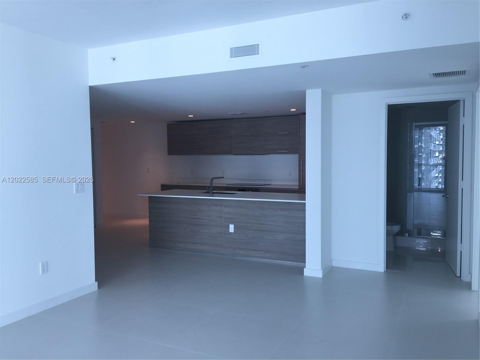 A modern kitchen features wood-toned cabinetry, a white island countertop, and light-colored tile flooring — 1300 S Miami # 1910, Miami FL 33130, MIAMI, FL