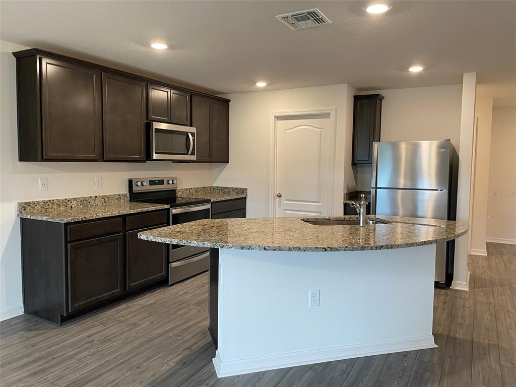 A kitchen features dark wood cabinets, granite countertops, stainless steel appliances, and a curved island — 1569 WYNFORD CIRCLE, TAVARES, FL