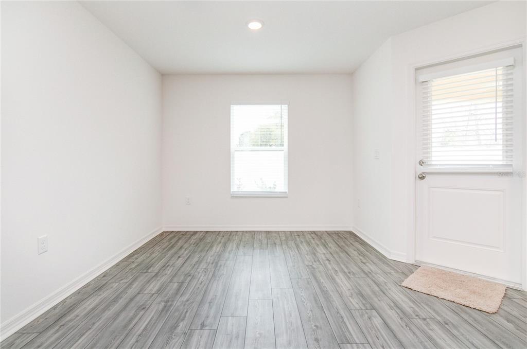An empty room features white walls, gray wood-look flooring, a single window, and a door — 1569 WYNFORD CIRCLE, TAVARES, FL