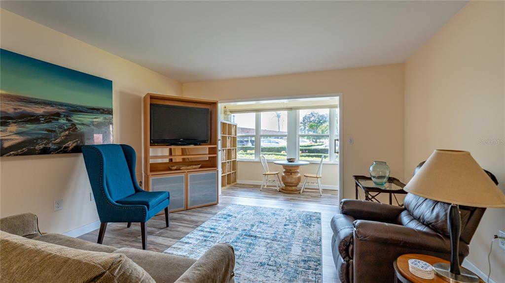 A living room features a blue armchair, a brown recliner, and a sunroom with dining furniture — 5020 BRITTANY DRIVE S UNIT 125, ST PETERSBURG, FL