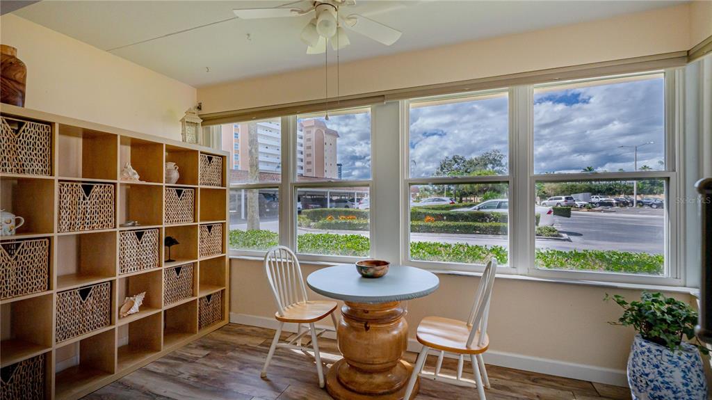 A sunroom features a wooden table, two chairs, a shelving unit, and large windows — 5020 BRITTANY DRIVE S UNIT 125, ST PETERSBURG, FL