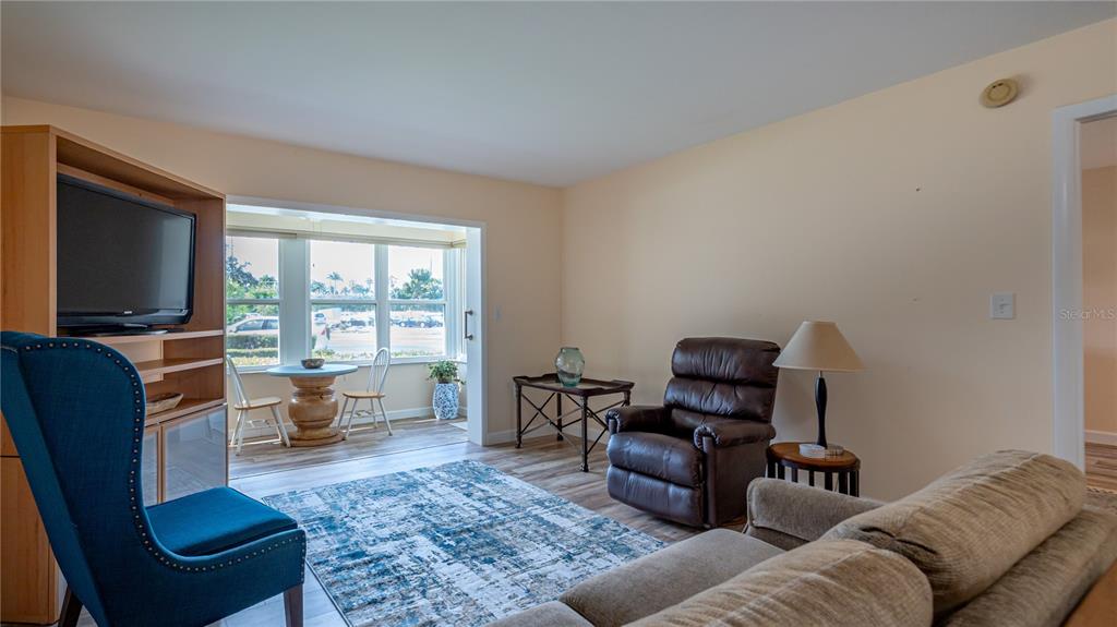 A living room features a blue armchair, a brown recliner, and a sunroom with windows — 5020 BRITTANY DRIVE S UNIT 125, ST PETERSBURG, FL