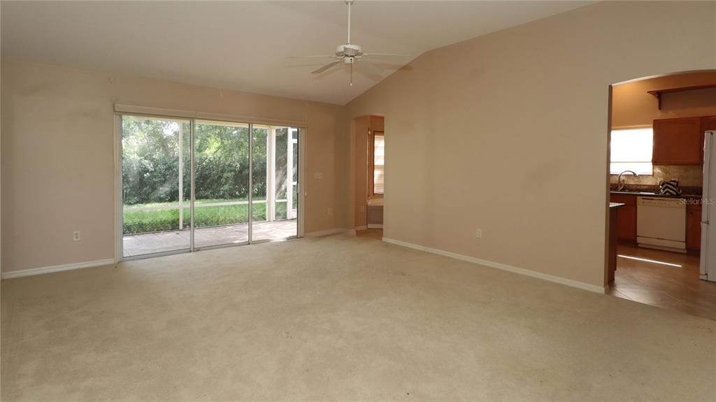 A living room with beige carpet, a ceiling fan, sliding glass doors, and an adjacent kitchen — 17700 SE 92ND GRANTHAM TERRACE, THE VILLAGES, FL