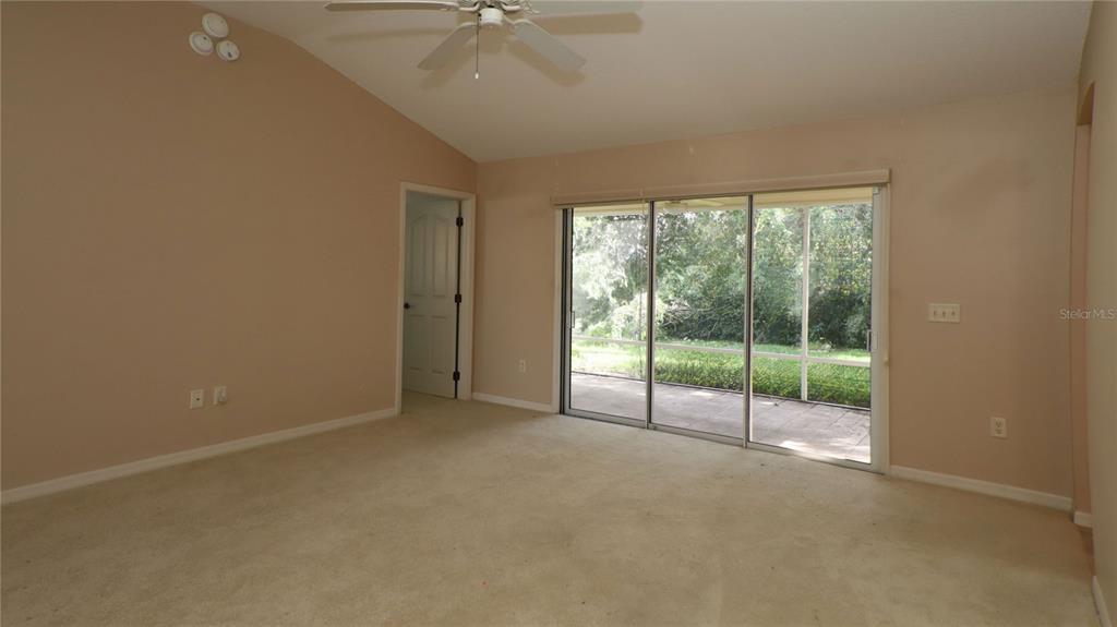 An empty room with beige carpet, tan walls, a ceiling fan, and sliding glass doors — 17700 SE 92ND GRANTHAM TERRACE, THE VILLAGES, FL