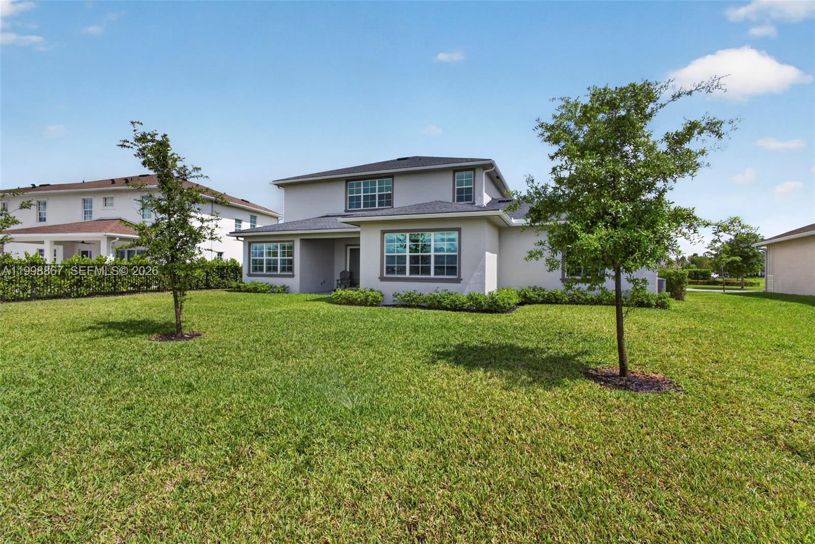 The exterior rear view of a two-story house features a lawn and two young trees — 769 Hookline Cir, Loxahatchee FL 33470, LOXAHATCHEE, FL