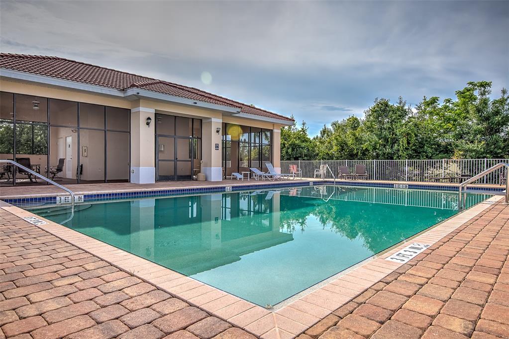 A rectangular swimming pool with brick pavers sits in front of a building with glass walls — 240 W END DRIVE UNIT 713, PUNTA GORDA, FL