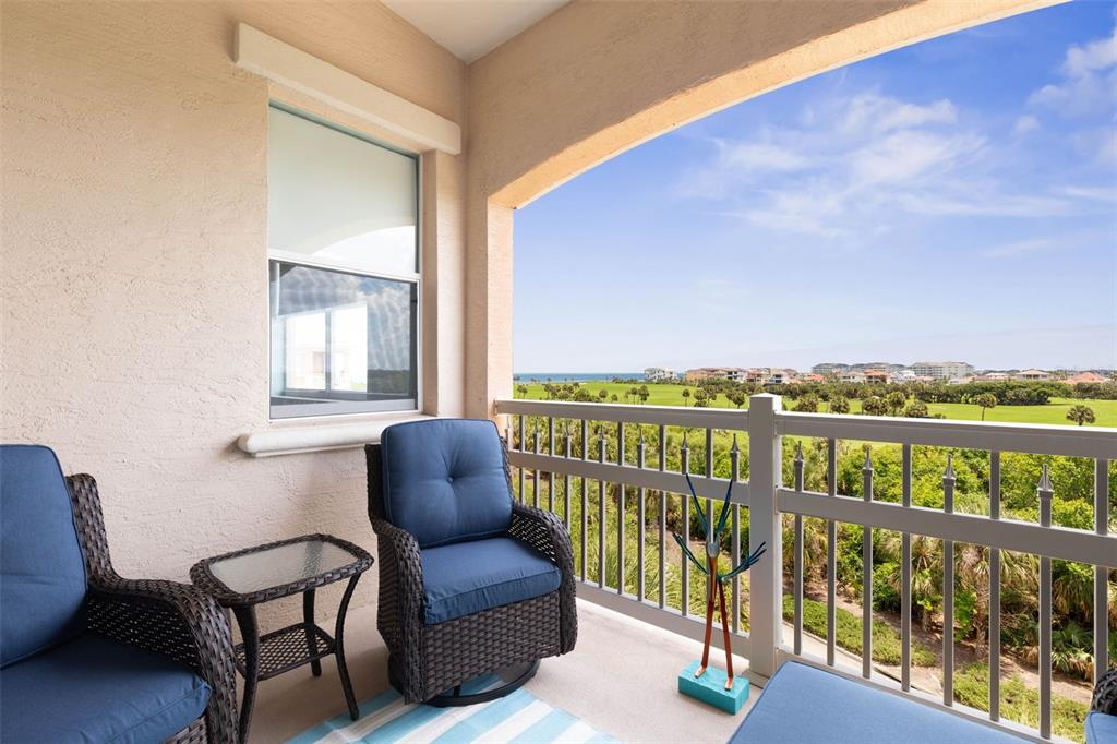 A balcony with wicker chairs and a small table overlooks a golf course and ocean — 25 OCEAN CREST WAY UNIT 1242, PALM COAST, FL