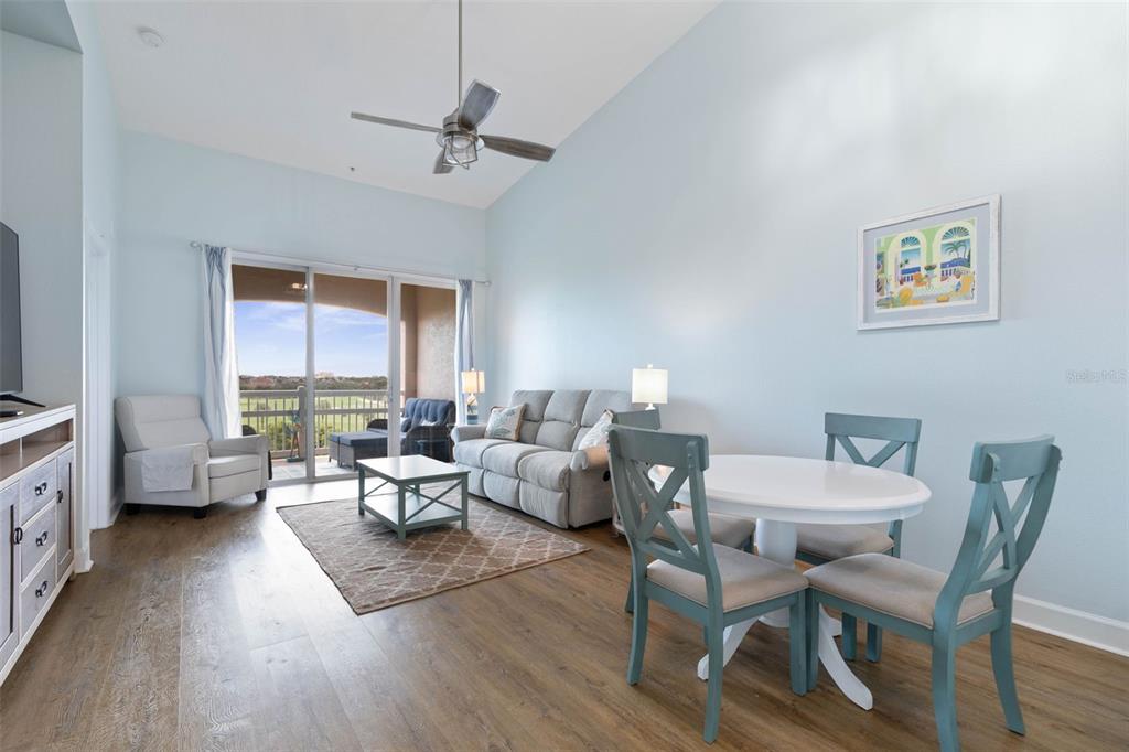 A living and dining area features light blue walls, wood-look flooring, and a balcony view — 25 OCEAN CREST WAY UNIT 1242, PALM COAST, FL